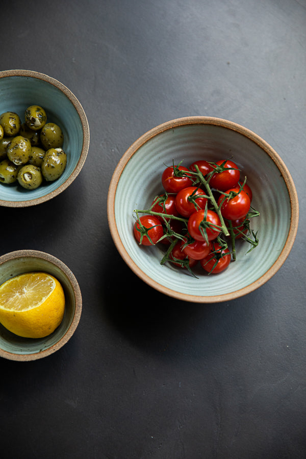 Handmade by the Leach Pottery Studio in St Ives. A set of three prepping bowls each one is glazed on the inside with a duck egg blue dolomite glaze. The outside is unglazed for a natural and organic feel. Displayed with food in each one in this image sitting on a dark grey background