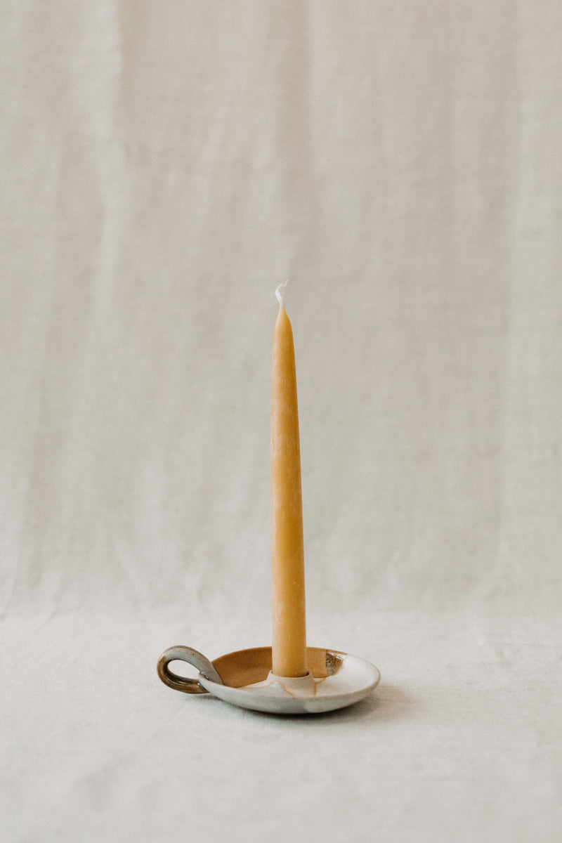 Handmade ceramic candle holder by Liz Vidal. This candle holder is a simple round shape and is finished with a small loop handle. Liz uses different tones of rust and brown glaze to dip her candle stick holders to create an abstract landscape design.