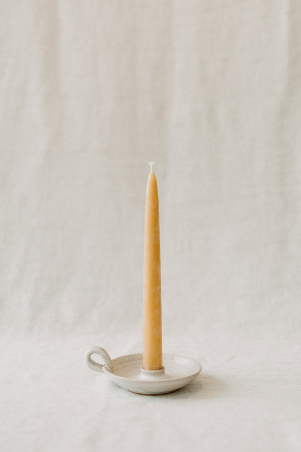 Handmade ceramic candle holder by Liz Vidal. This candle holder is a simple round shape and is finished with a small loop handle. Liz has used a plain white glaze which shows small specs from the clay though it, giving it a beautiful natural finish.