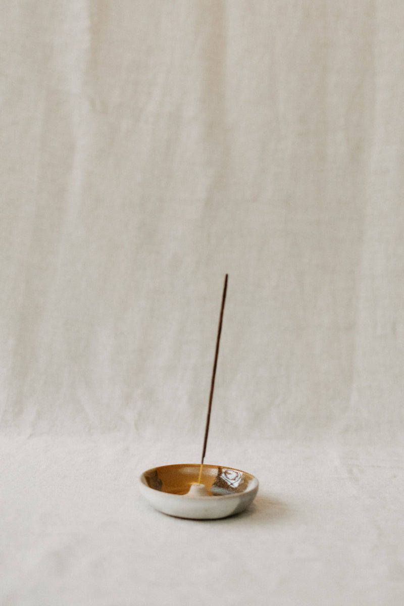 Handmade ceramic incense holder by Liz Vidal. This incense holder is a simple round shape and is finished with a hole for the incense to stand in. Liz uses different tones of rust and brown glaze to dip her incense holders to create an abstract landscape design.