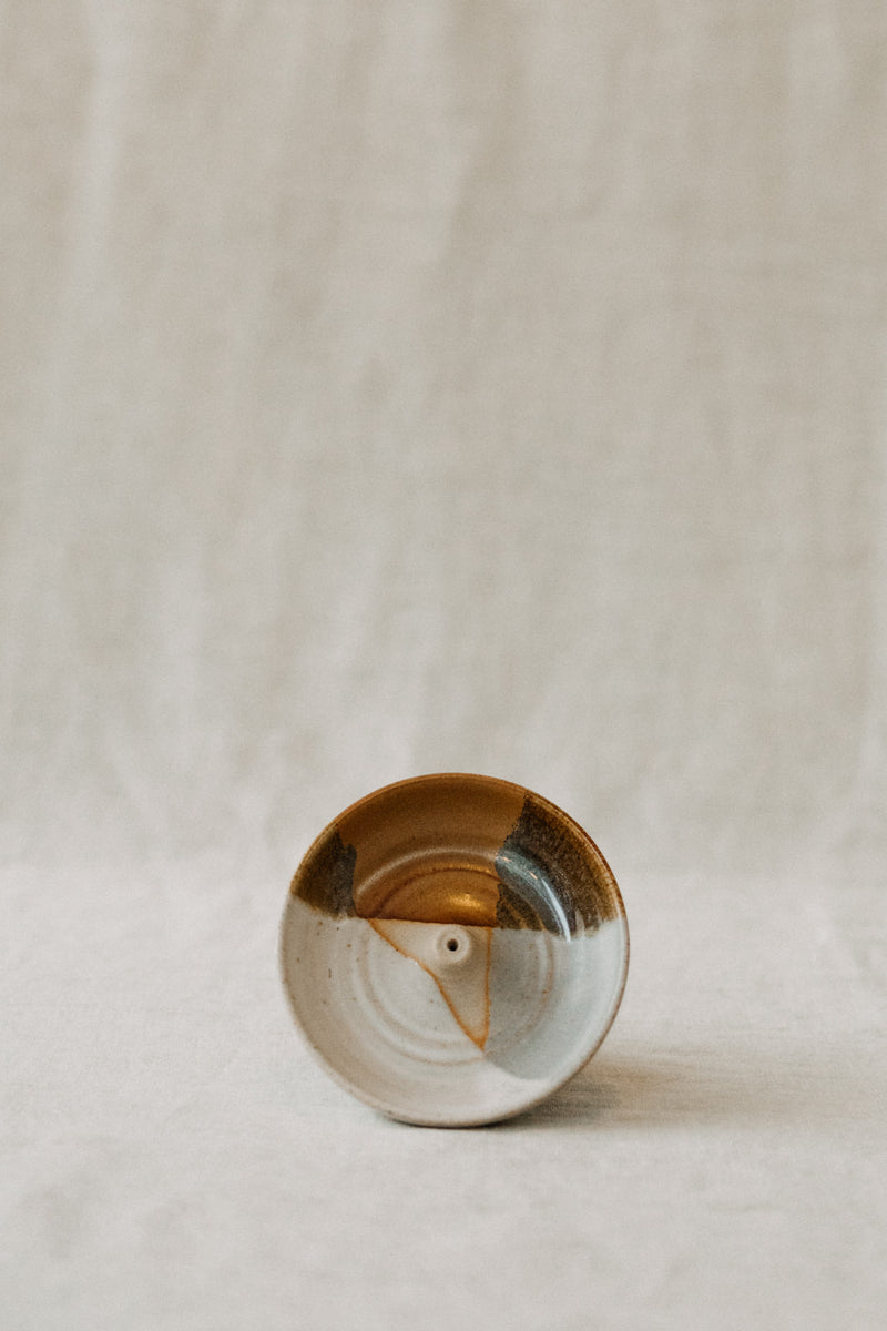 Handmade ceramic incense holder by Liz Vidal. This incense holder is a simple round shape and is finished with a hole for the incense to stand in. Liz uses different tones of rust and brown glaze to dip her incense holders to create an abstract landscape design.