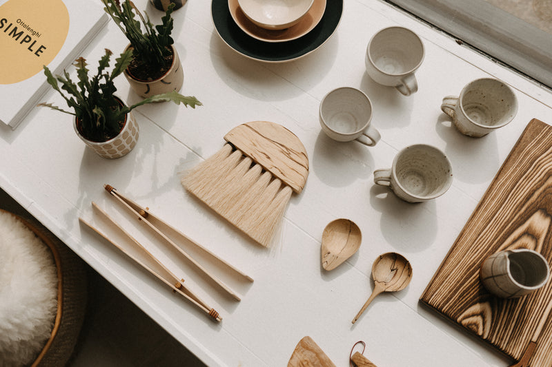 Small hand carved multi purpose scoop made from sustainably sourced wood. shallow scoop and a delicate long handle. Displayed with other handmade objects on a shelf.