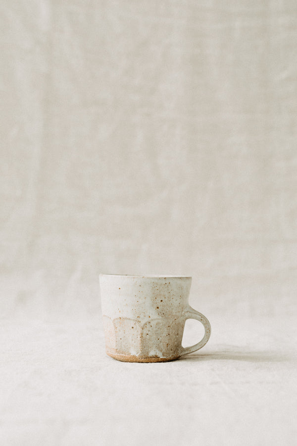 Small Handmade ceramic cup by Tim Lake. Made with a low handle and faceted at the bottom edge. Glazed with a rust FFM glaze