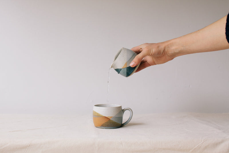 Handmade ceramic jug by Liz Vidal. Liz uses different tones of rust and brown glaze to dip her jugs to create an abstract landscape design. Pictured here pouring from the jug into the cup