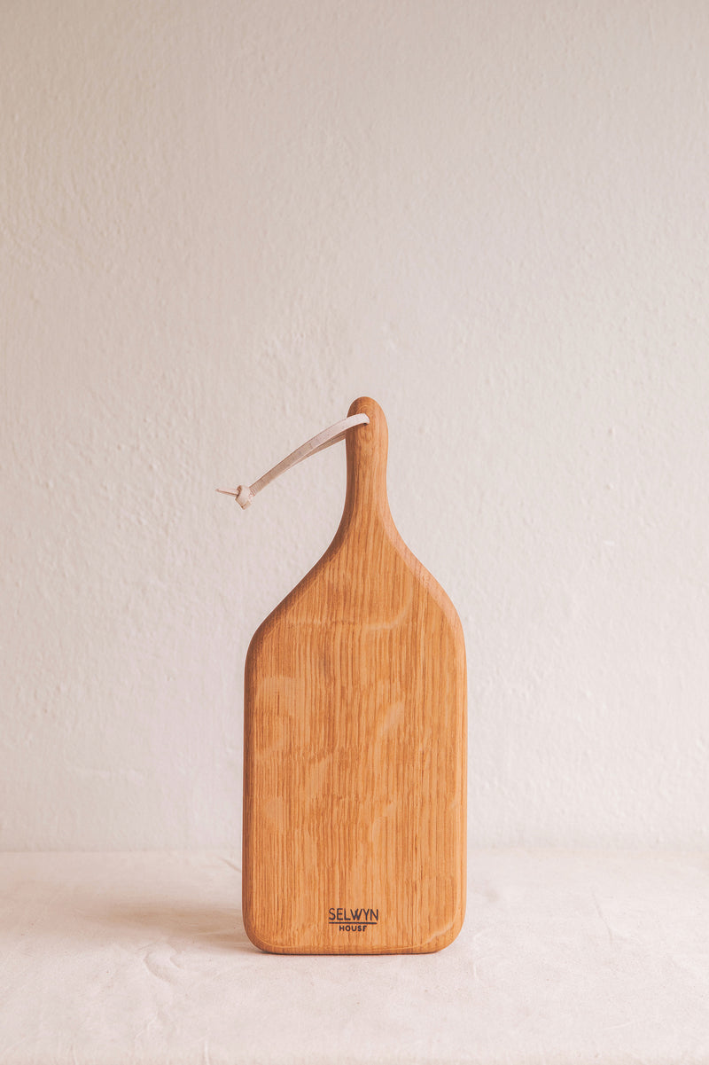 Handmade small oak chopping board by Selwyn House. A rectangle shape with slightly rounded corners and carved with a handle with a hole and leather loop in the end for easy storage and hanging.